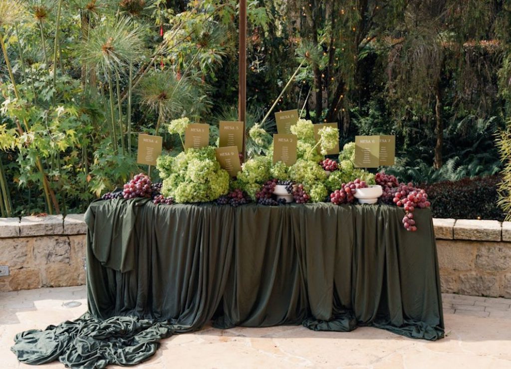 Mesa editorial con tela drapeada verde oliva, uvas y flores verdes